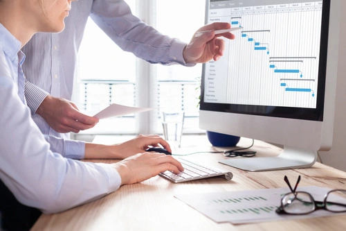 Two people in front of a computer showing a Gantt chart